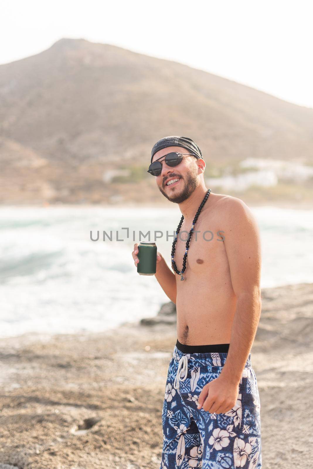 Male young adult in swimsuit posing happily with a drink on the beach, portrait, foggy background