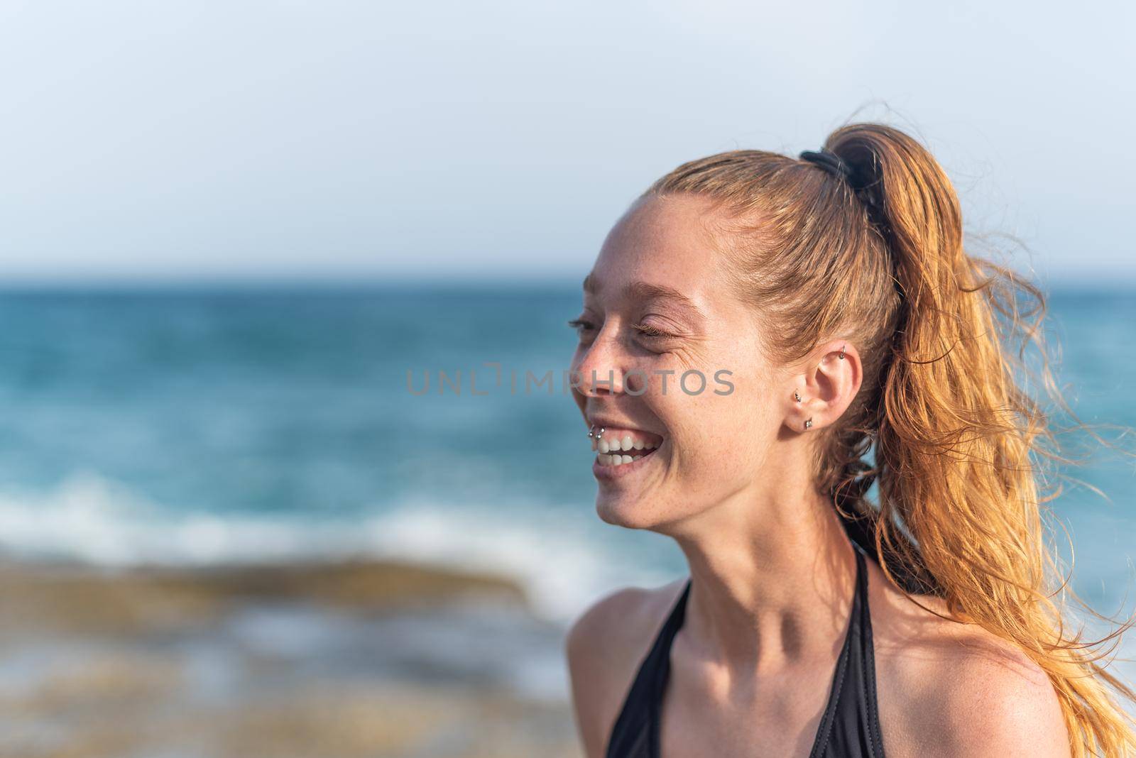 redhead woman with ponytail on the beach laughing, side portrait