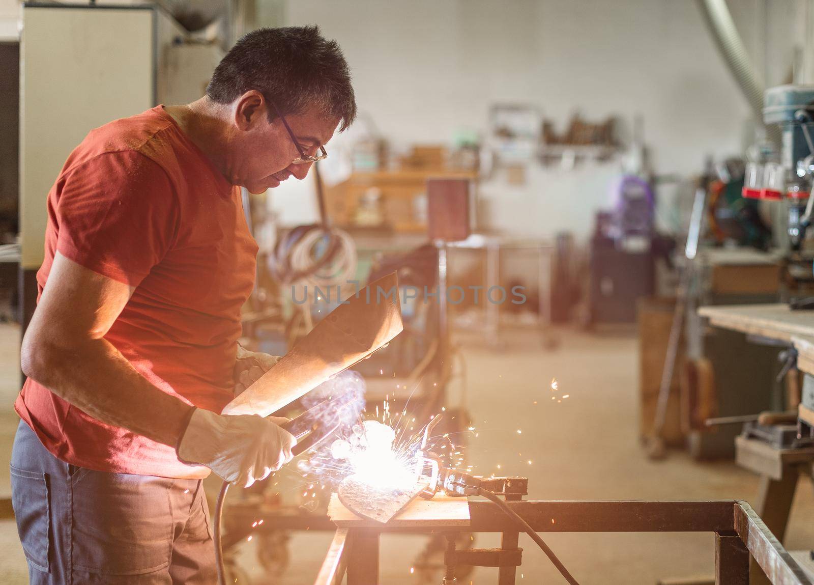 Person in red T-shirt and glasses welding with a shield, sparks, horizontal