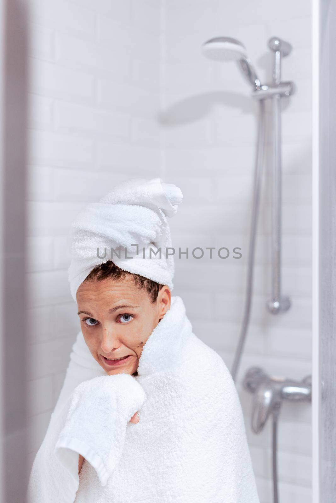 An adult caucasian woman comes out of the shower after taking a hot shower with a towel and very cold looking at the camera. Concept of hotel room.