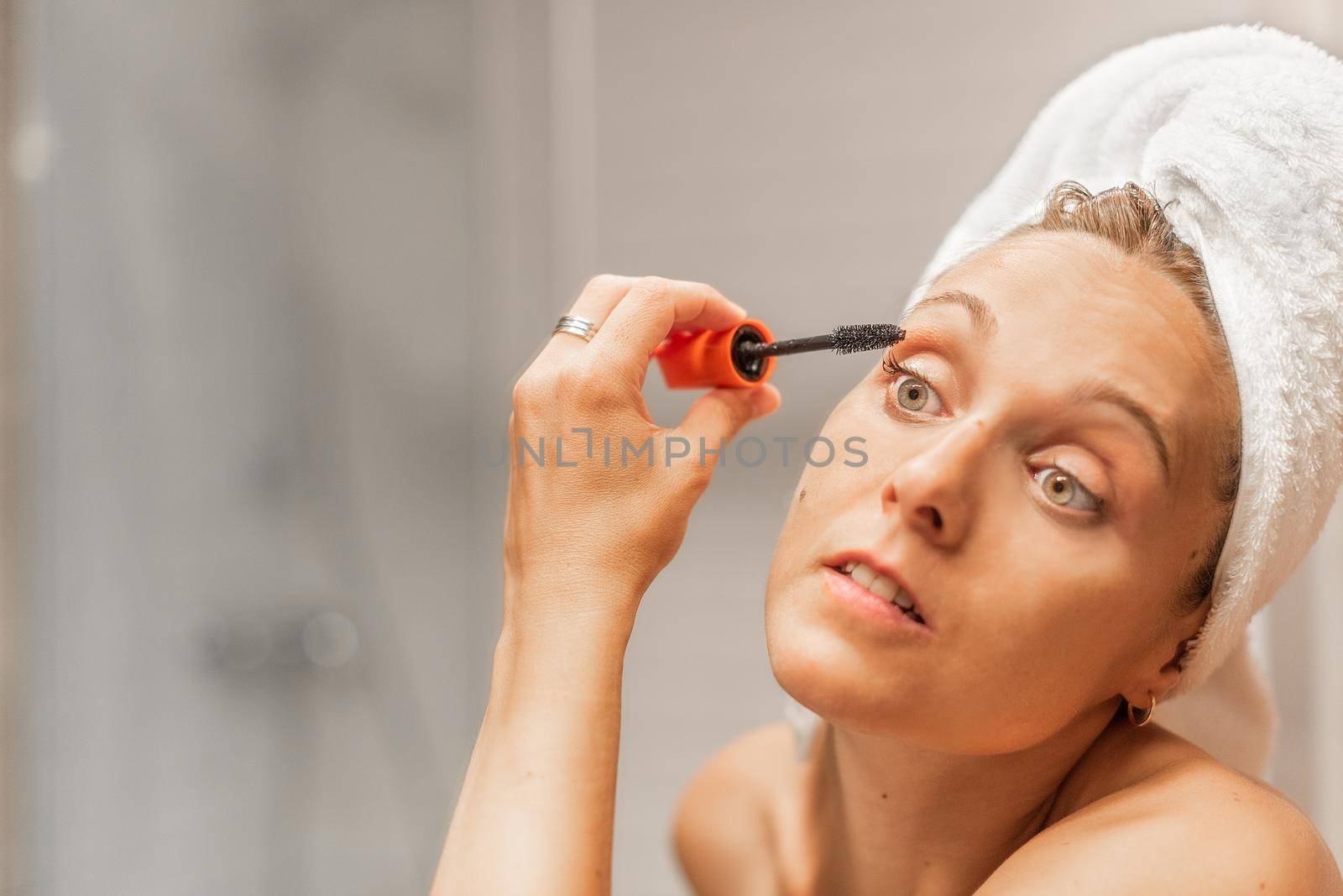 Close up view of an adult woman applying mascara on eyelash in bathroom of a hotel while looking in the mirror with copy space. Concept of beauty.