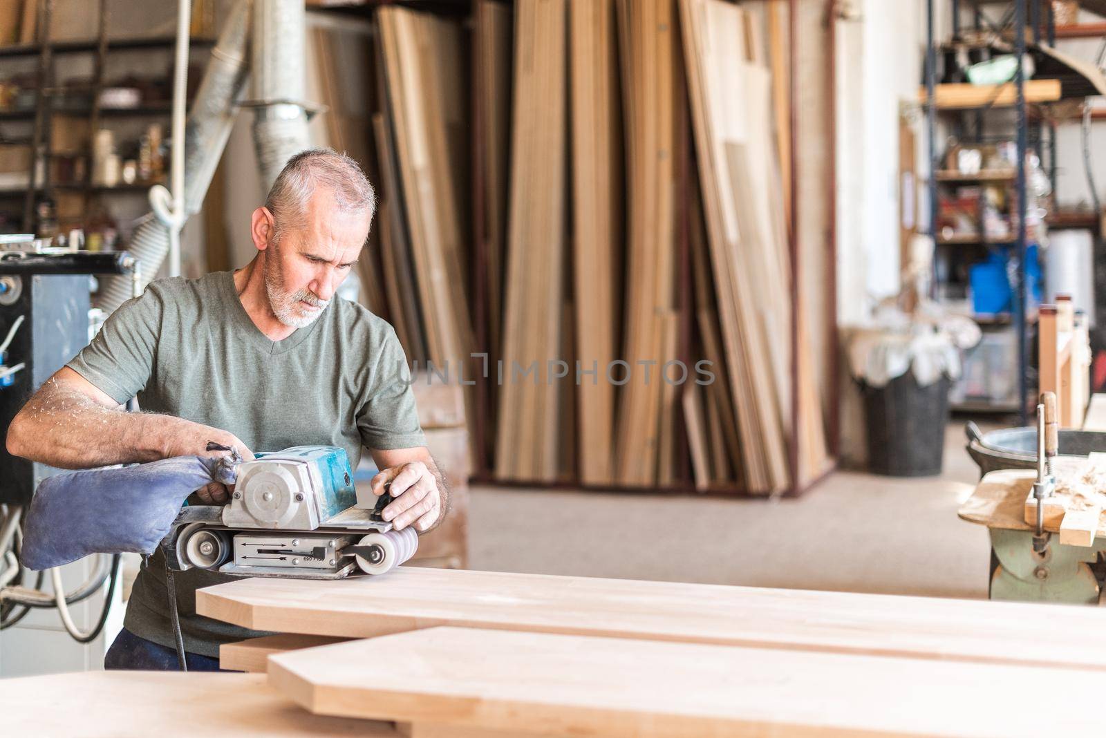 Man standing with a hand sander polishing a wooden board, horizontal view