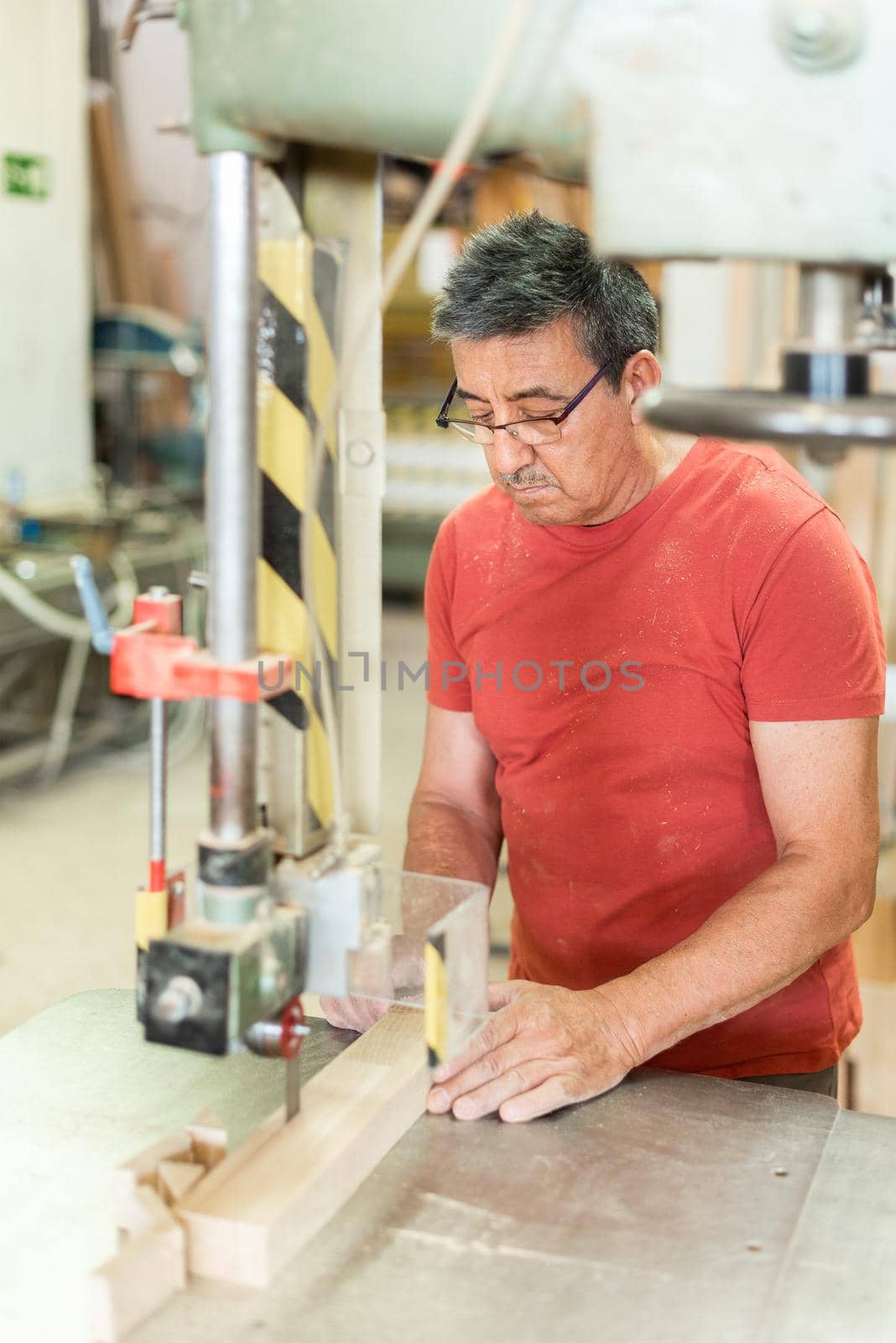 Man focused cutting a wooden board with a band saw, vertical foreground, blurred background