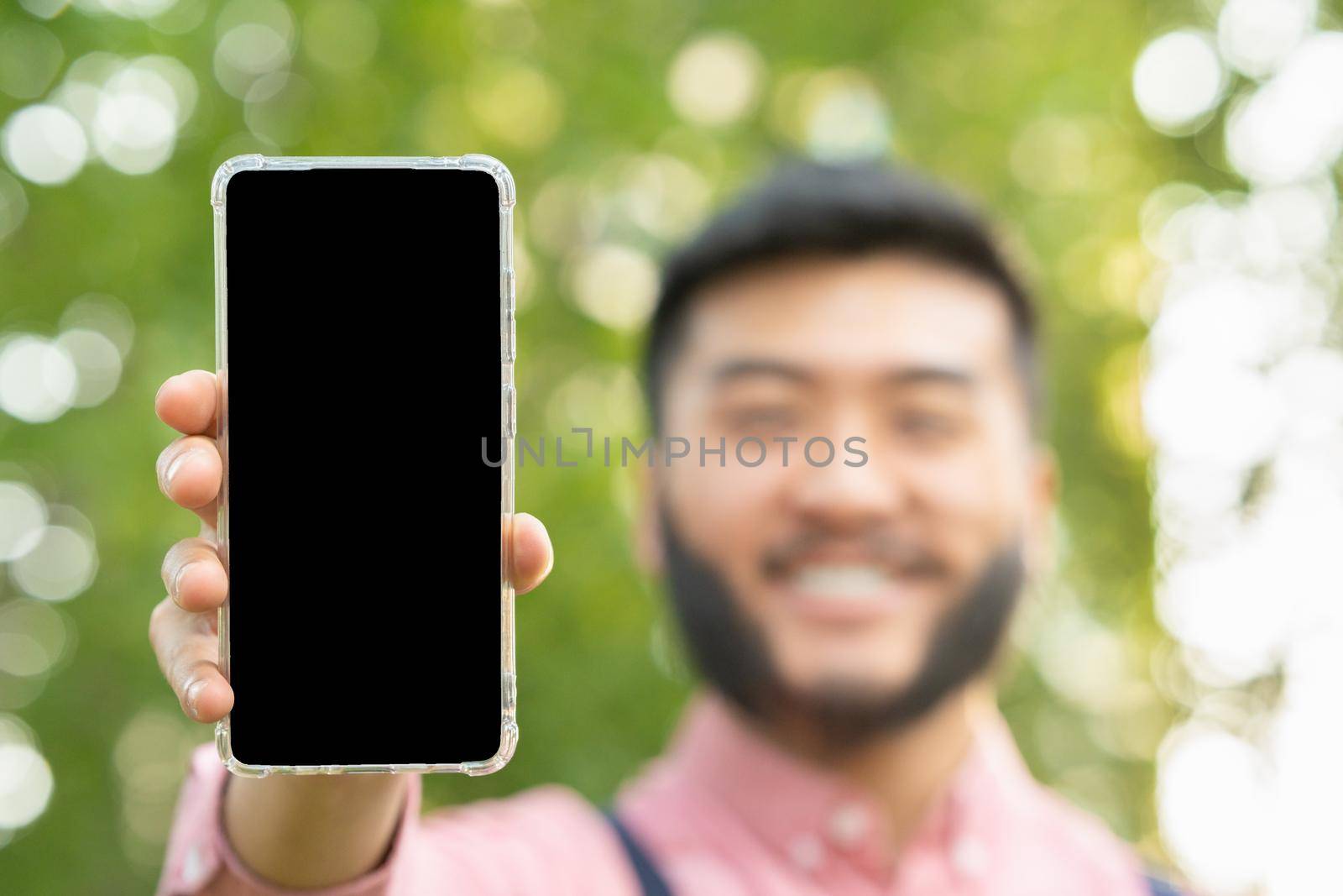 Selective focus on the screen of a mobile phone showing an asian man in casual clothes in a park