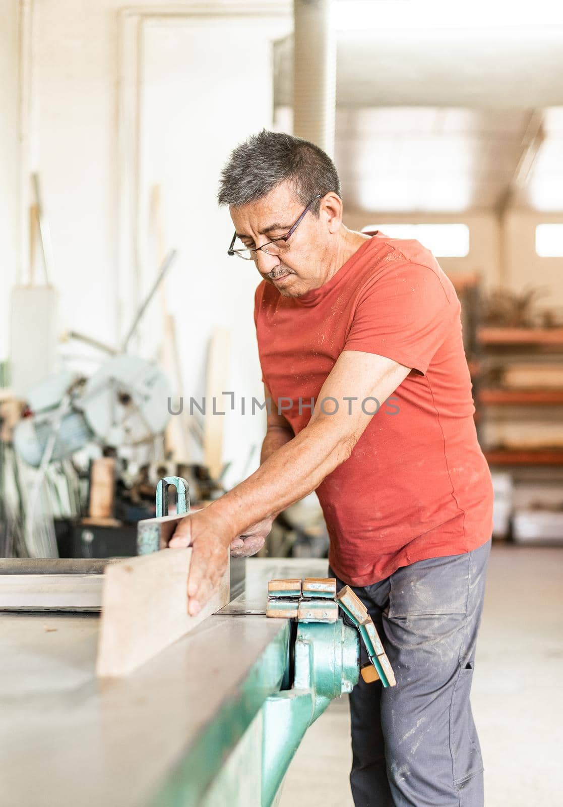 Adult man focused working manually with a wood planing machine, blurred vertical background