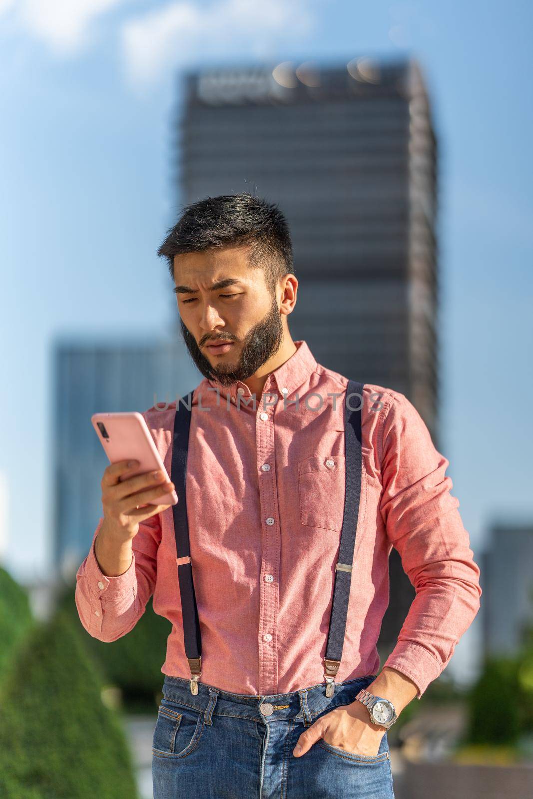 Vertical photo of aserious asian businessman in shirt and braces using mobile with in the city