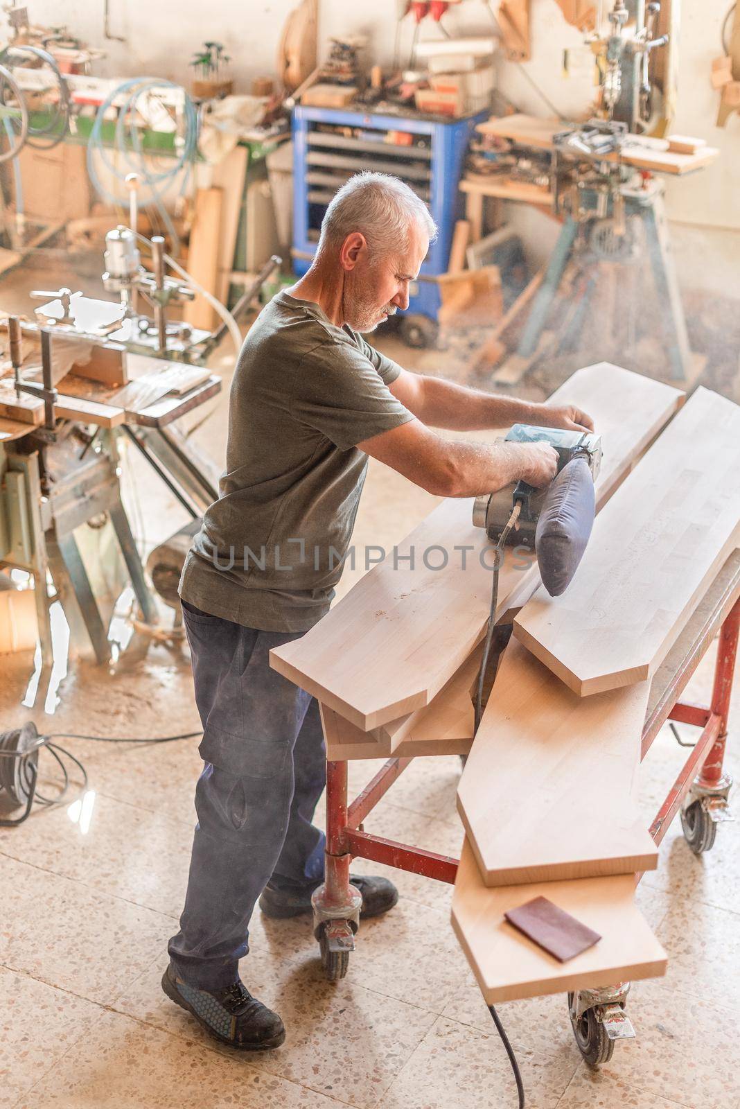 Man working with a hand sander polishing a wooden board, vertical