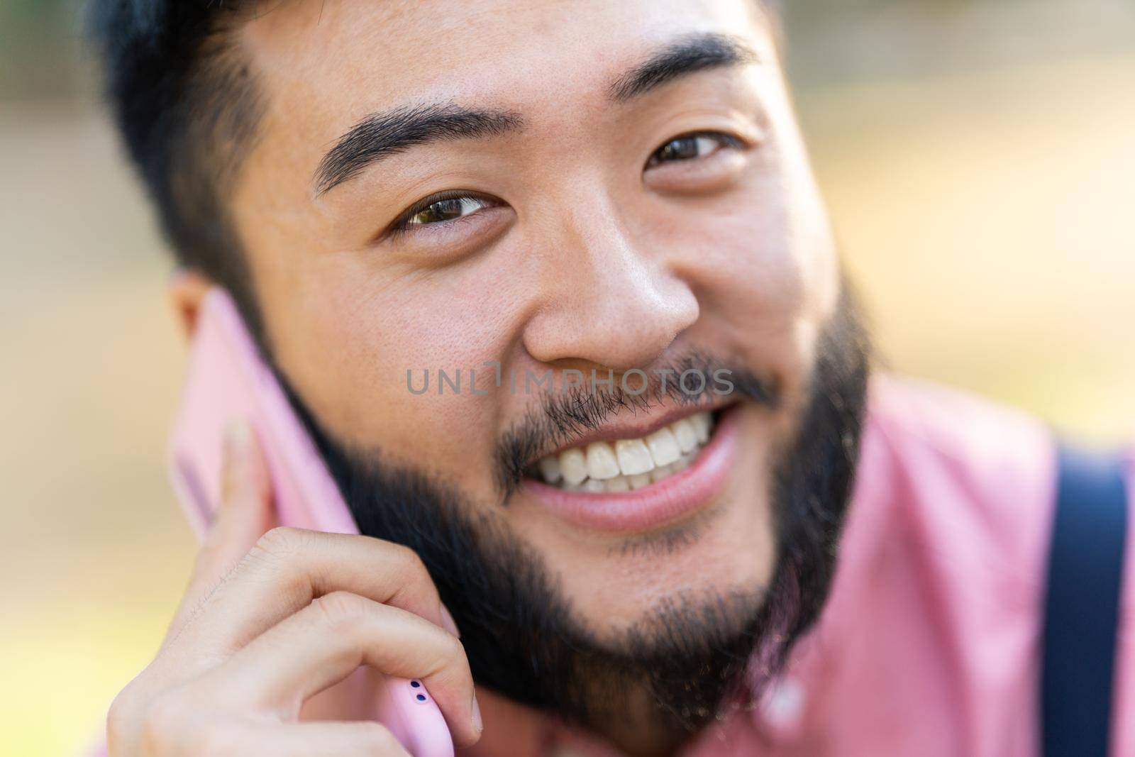 Close up portrait of a chinese man in casual clothes smiling while talking to a mobile outdoors