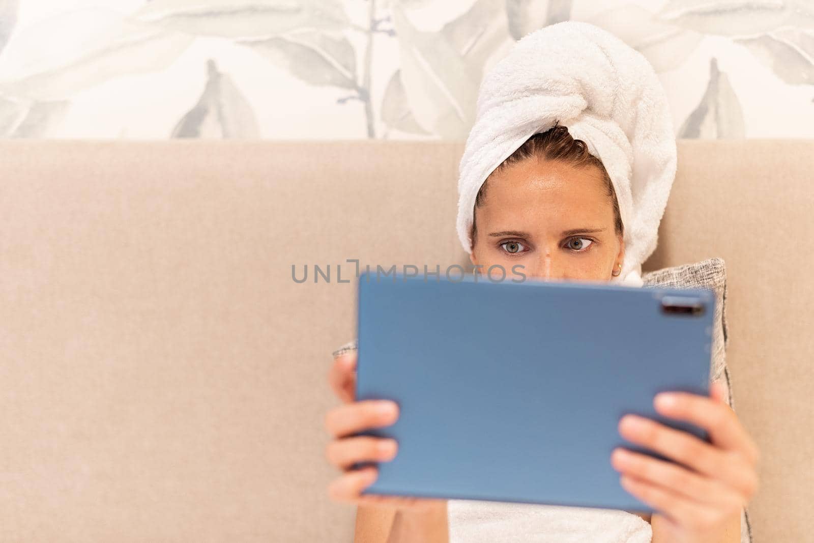 Front view of a woman wrapped in towels using her digital tablet in the bedroom of a hotel with copy space. Concept of vacation, hotel.