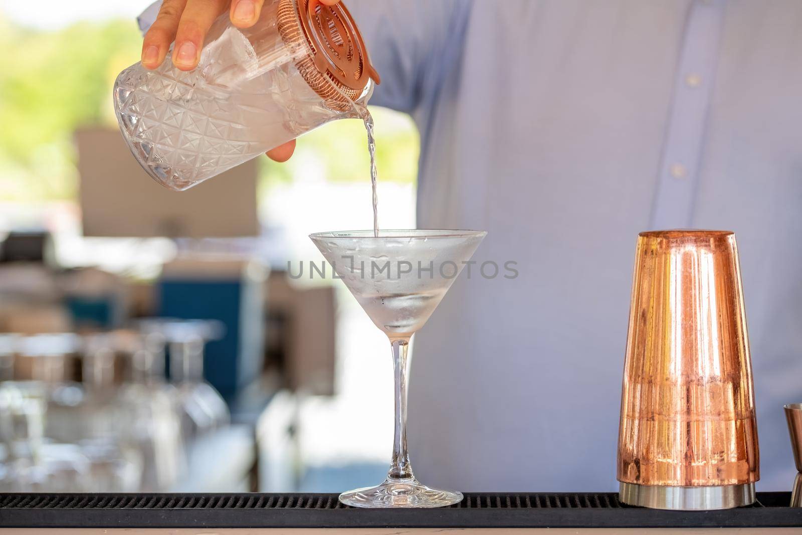 Professional bartender pouring cocktail into glass glass with shaker