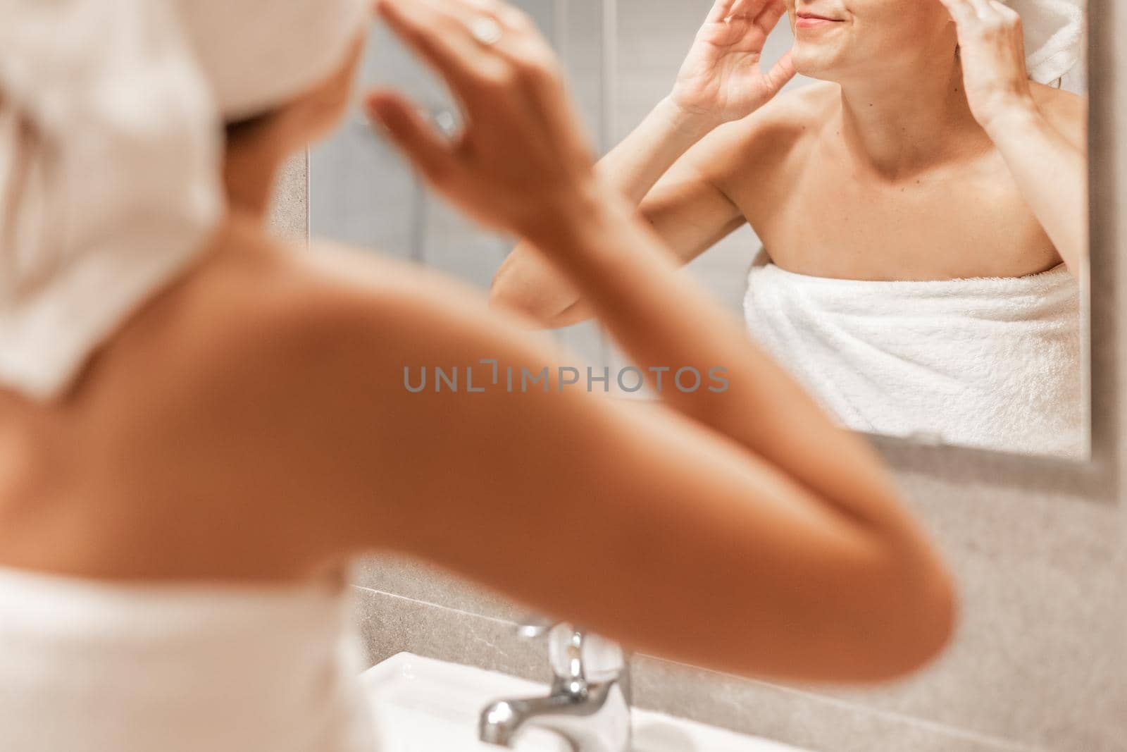 An unrecognizable adult woman looking in the mirror after taking a bath and massaging her face in a hotel bathroom. Concept of skin care.