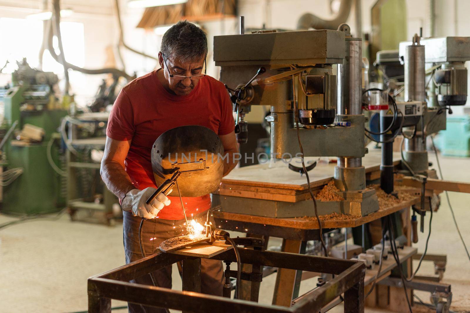 Person in red T-shirt welding in a manufacturing plant, horizontal