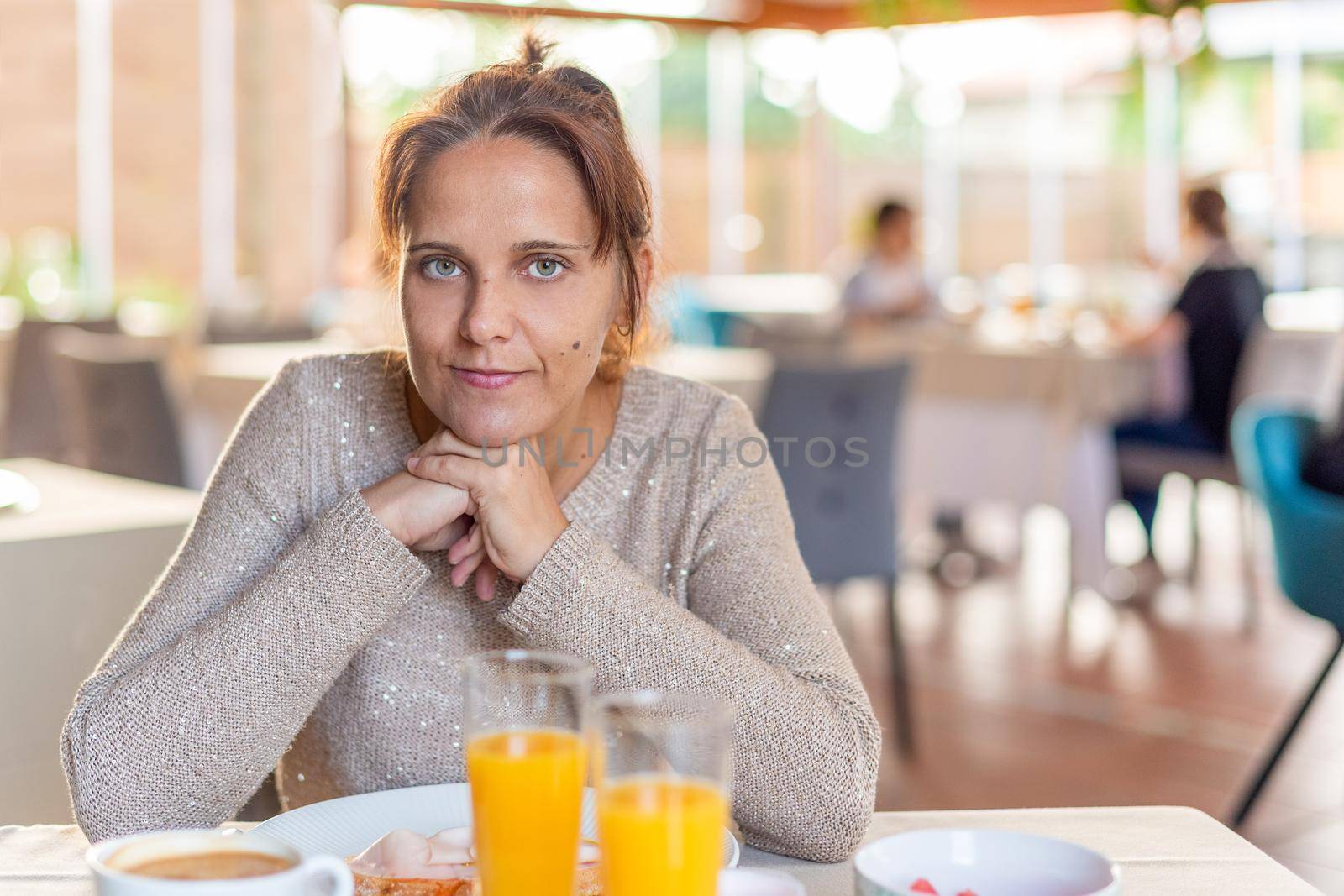 Front view of an adult woman having breakfast in hotel where she is staying while looking at the camera. Concept of breakfast in hotel.