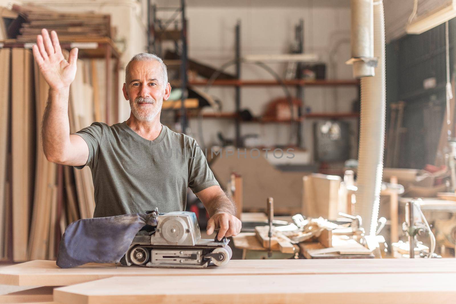 Smiling worker waving with a hand sander machine by ivanmoreno