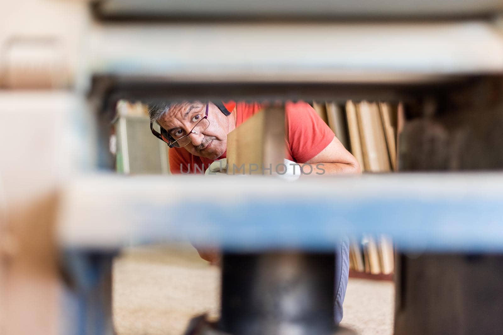 Male adult in red T-shirt and glasses working with a wood planer, background in focus