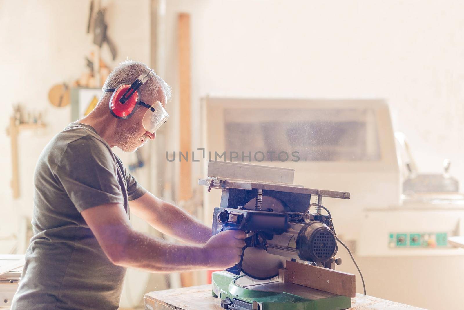 person working with a miter saw in safety equipment, light background