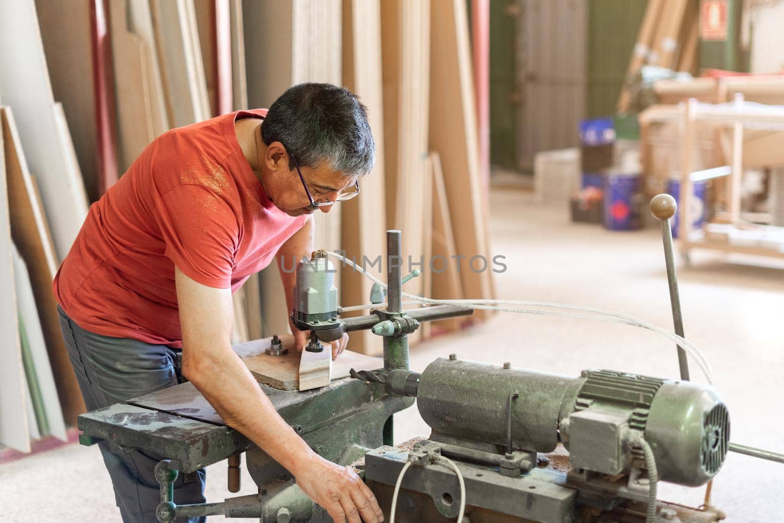 Male adult with glasses and red t-shirt drilling wood by ivanmoreno