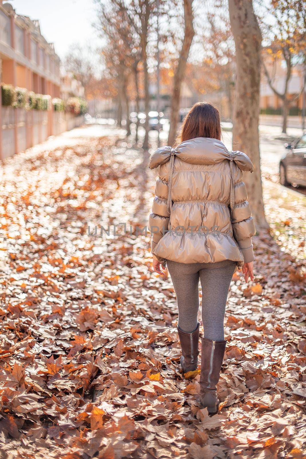 woman walking in the street full of fallen leaves by ivanmoreno