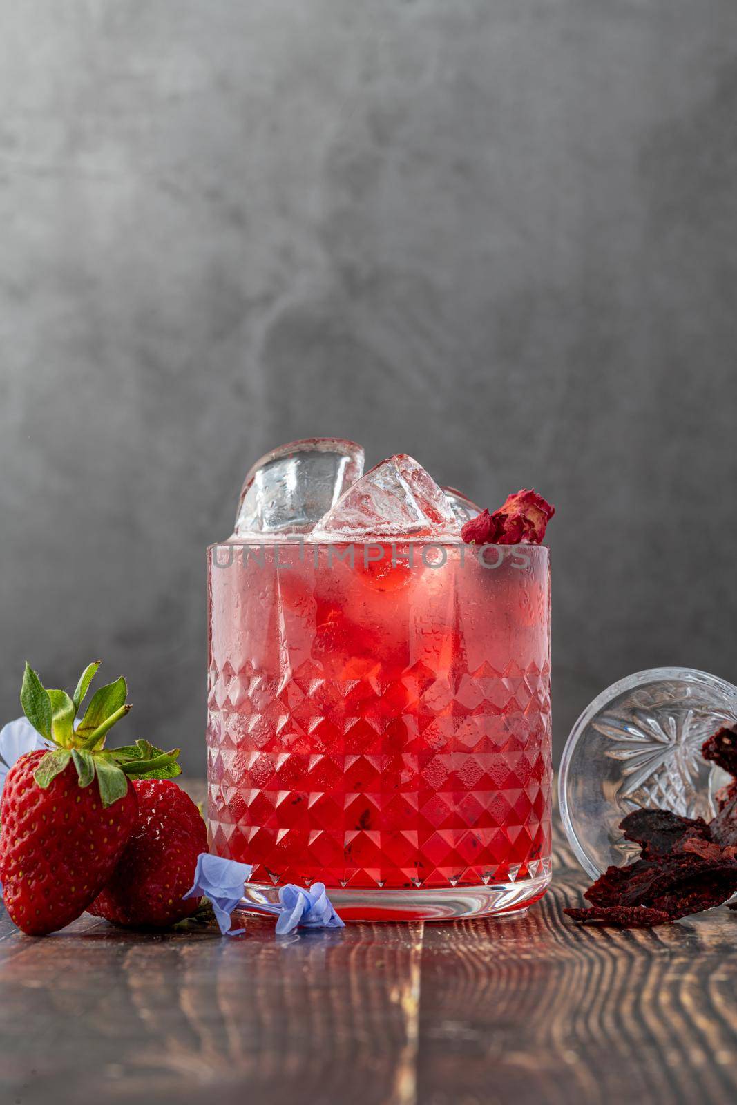Iced cold strawberry tea with slices of dried strawberries on wooden table by Sonat