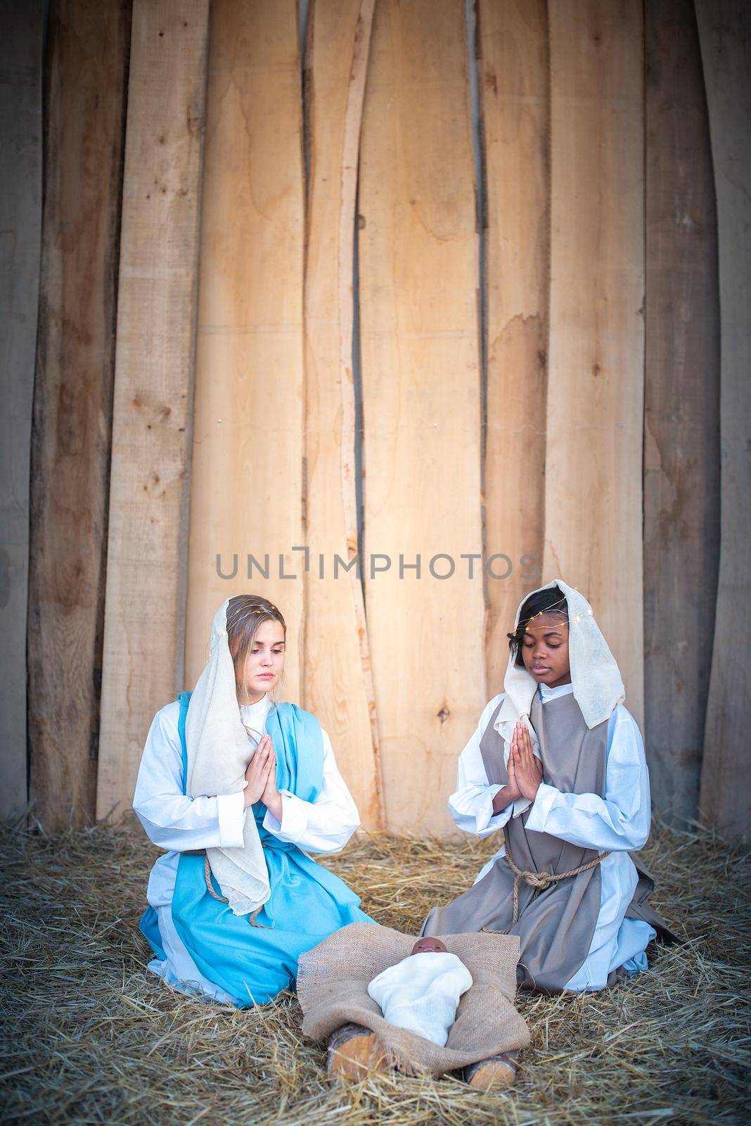 Vertical photo of lgtb nativity scene with two virgin marys praying next to an african Jesus baby