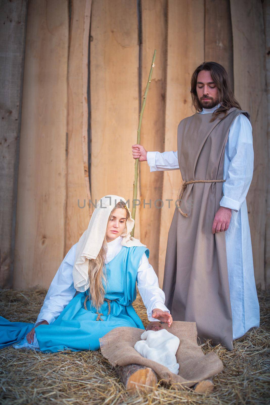 Vertical photo of a nativity scene with the virgin mary and joseph adoring the baby jesus in a crib