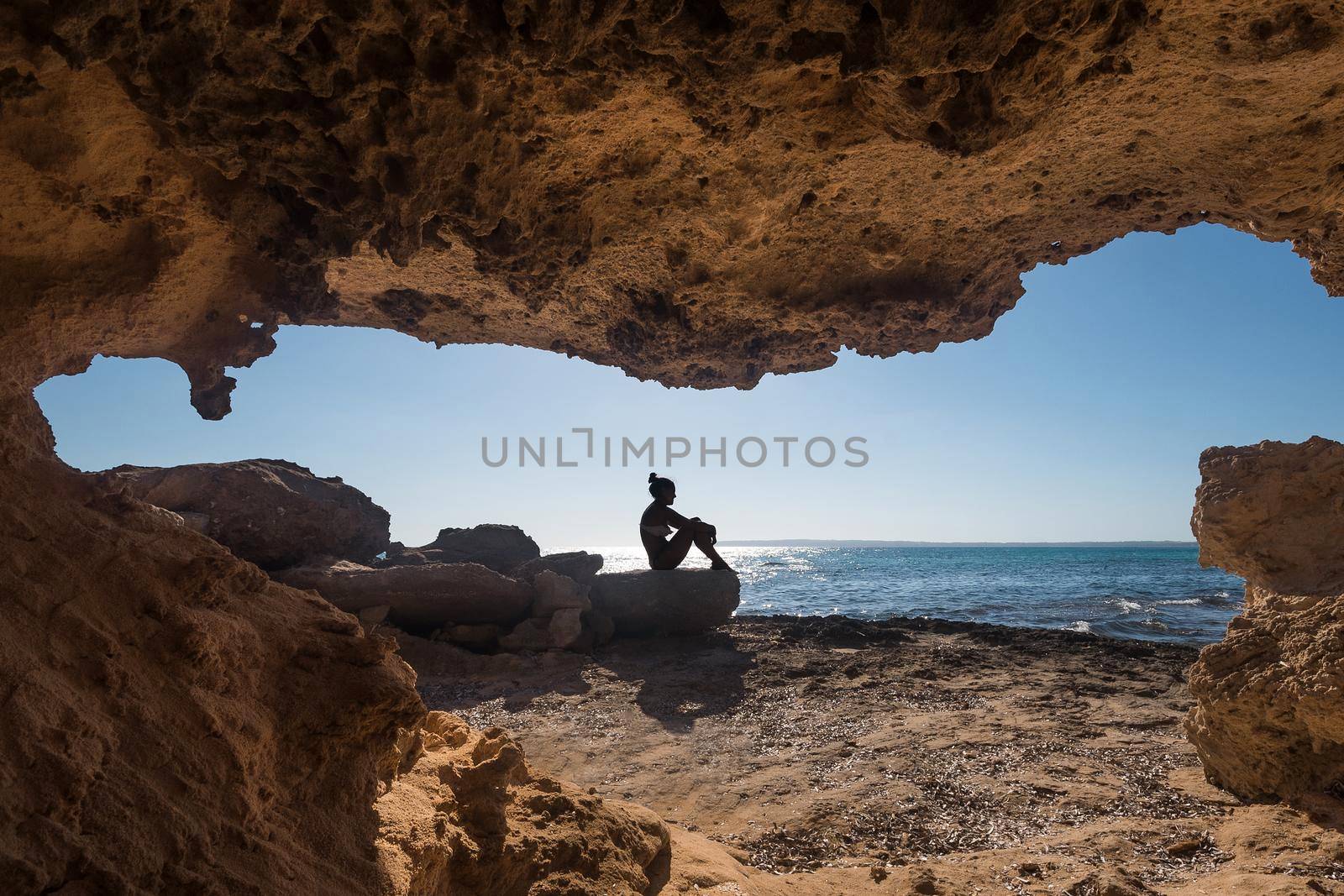 Woman sitting next to a cave near the sea by ivanmoreno