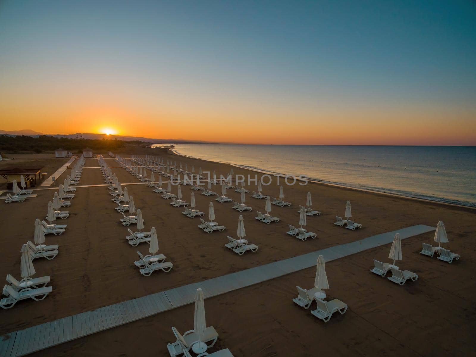 Aerial view of parasols and sun loungers on calm sea beach at sunrise