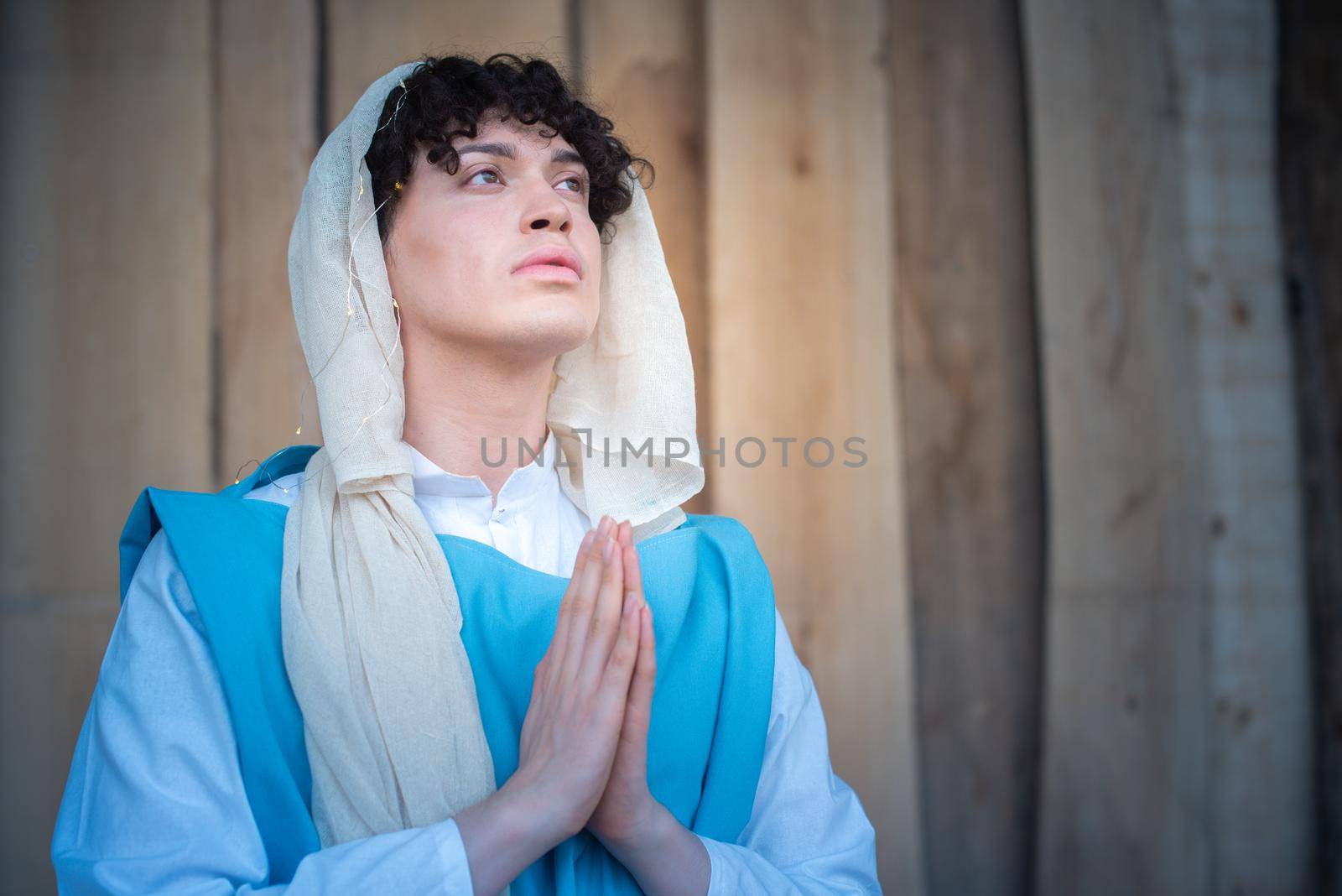 Vertical portrait of an androgynous virgin mary praying while looking up with relaxed expression