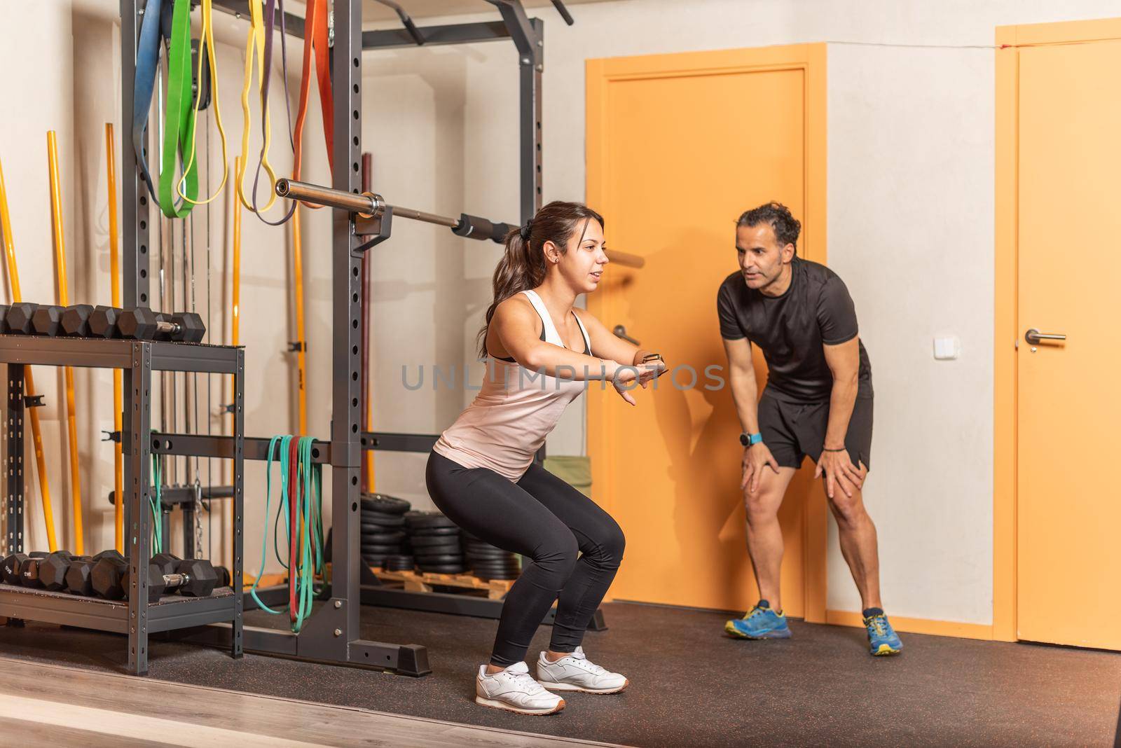 Sportswoman doing squats without weighting exercise with trainer in gym. Concept of gym.