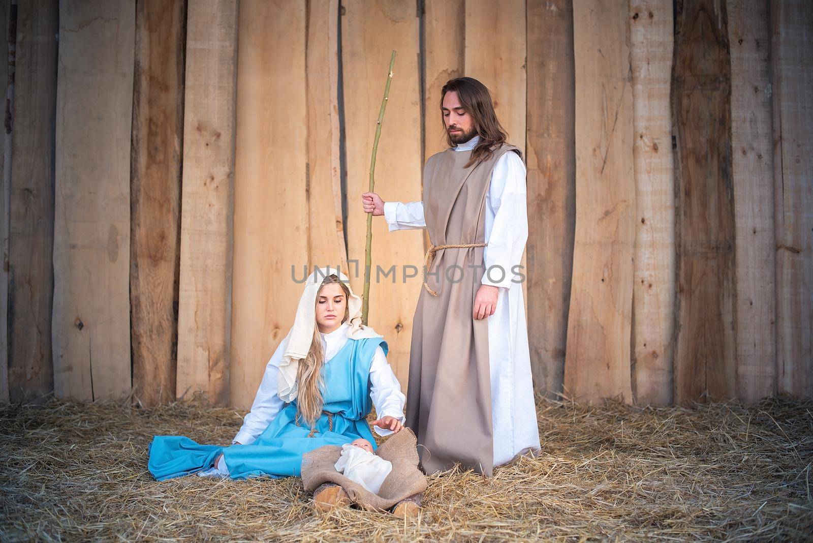 Traditional nativity with the virgin mary seated next to baby jesus and Joseph standing in a crib