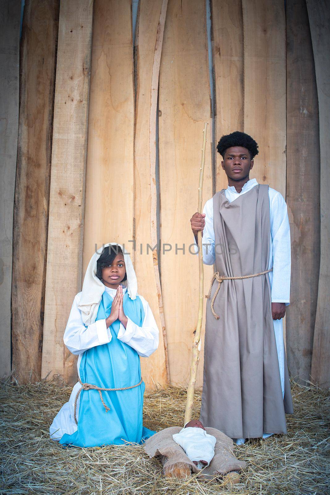 Vertical portrait of black virgin mary and black joseph praying next to jesus baby in a crib