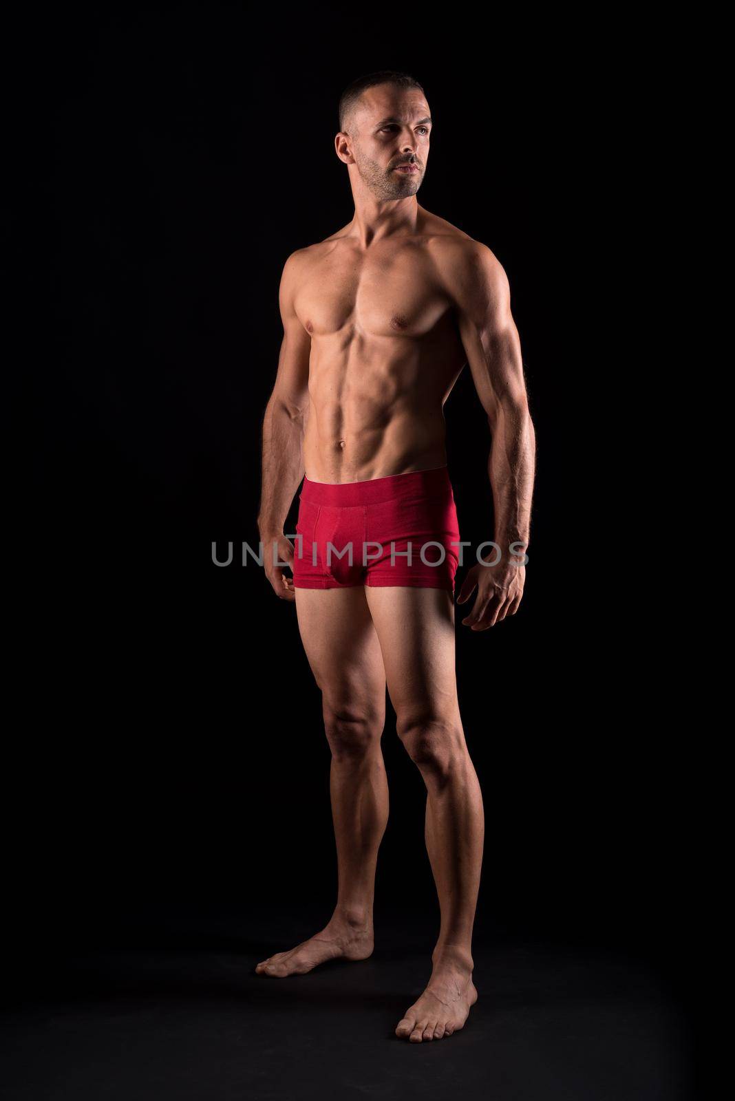 Vertical studio portrait of a strong adult male in pants standing distracted with black background