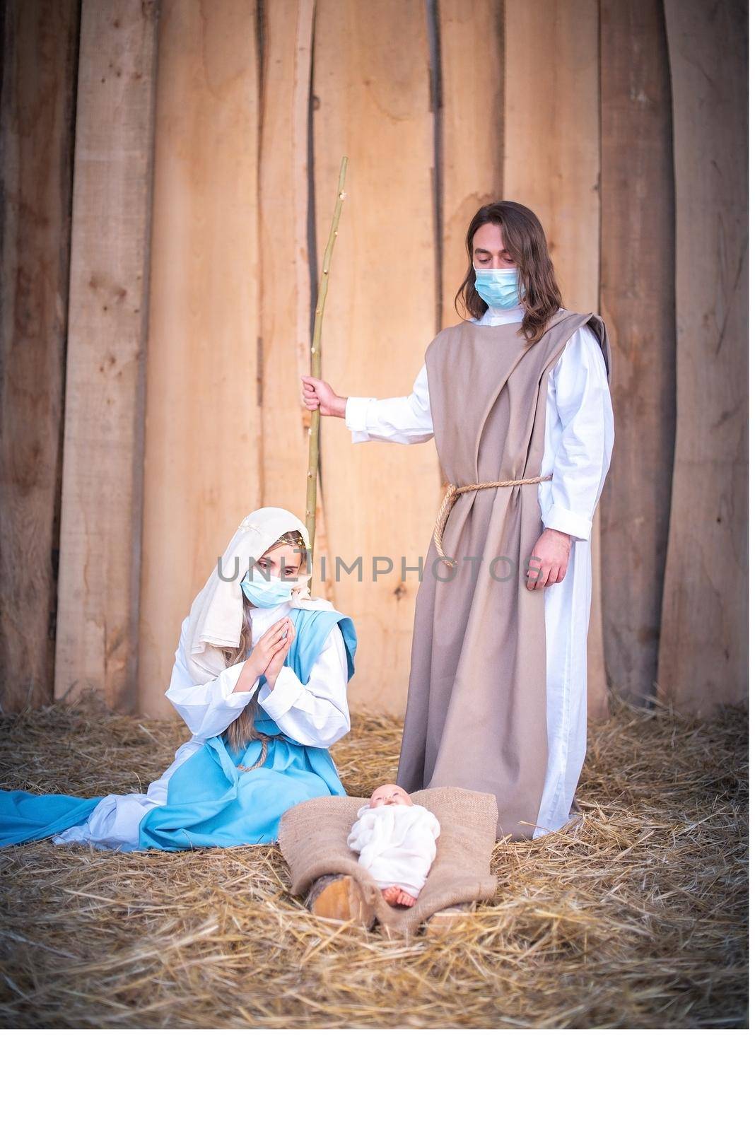 Vertical photo of a nativity scene with the characters wearing masks while adoring Jesus baby