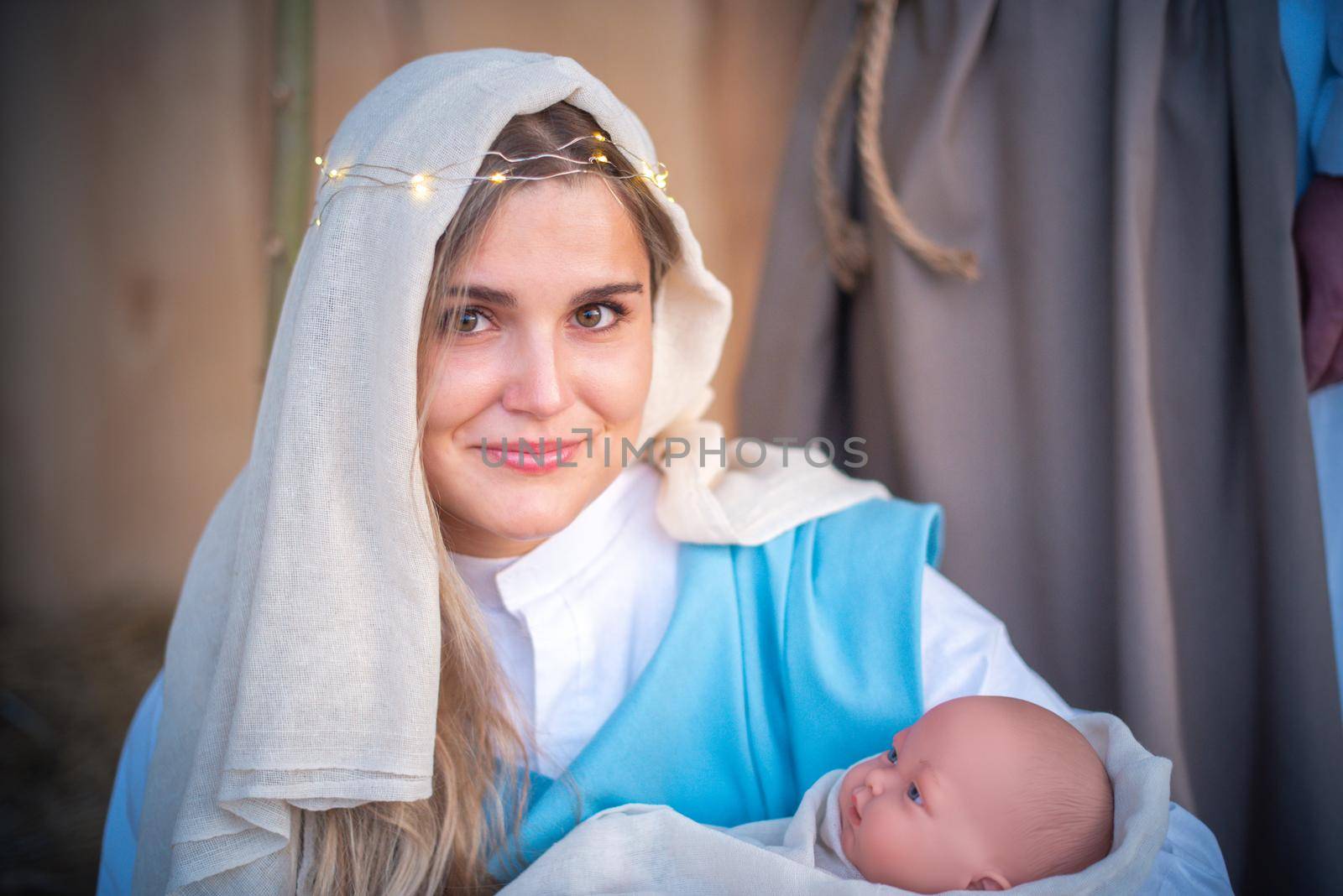 Caucasian woman representing virgin mary facing the camera and holding Jesus baby in arms in a crib