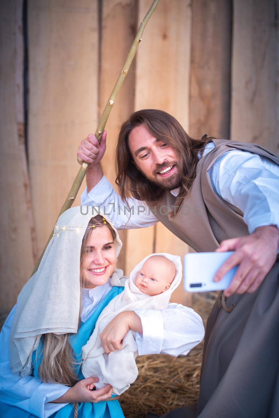 Vertical photo of characters of the virgin mary and joseph taking a selfie while smiling in a crib