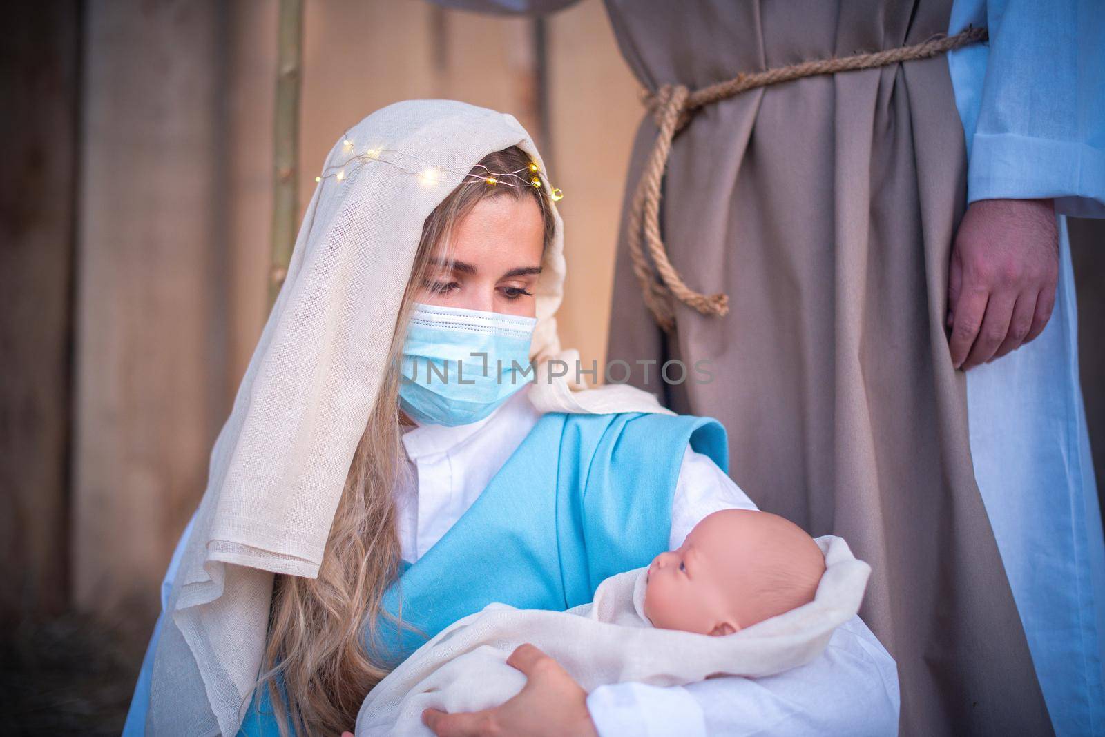 Caucasian woman with mask representing virgin mary holding Jesus baby in a nativity scene