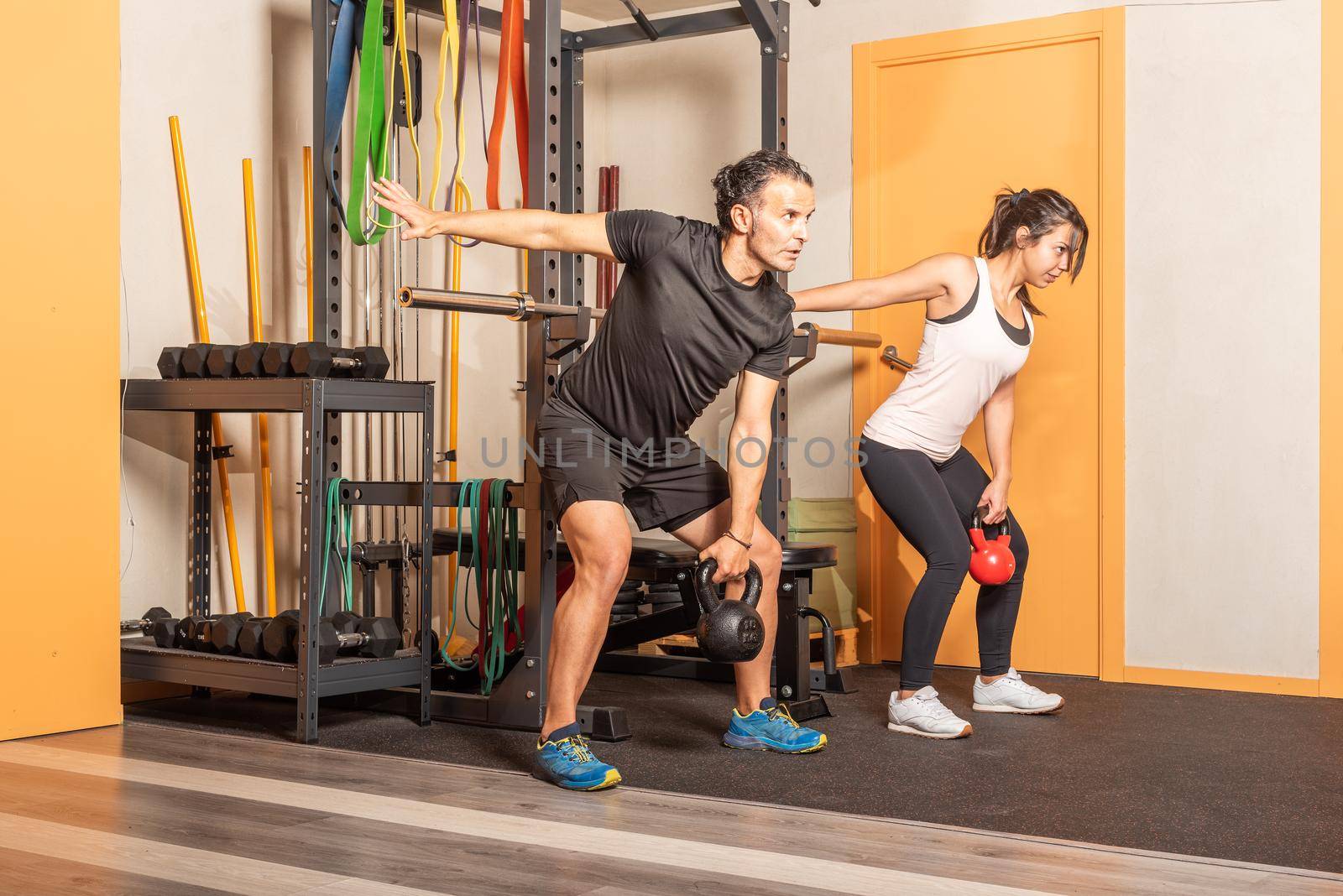 Sporty woman and man doing shoulder press exercises with kettlebells in gym. Concept of exercises with equipment in gym.