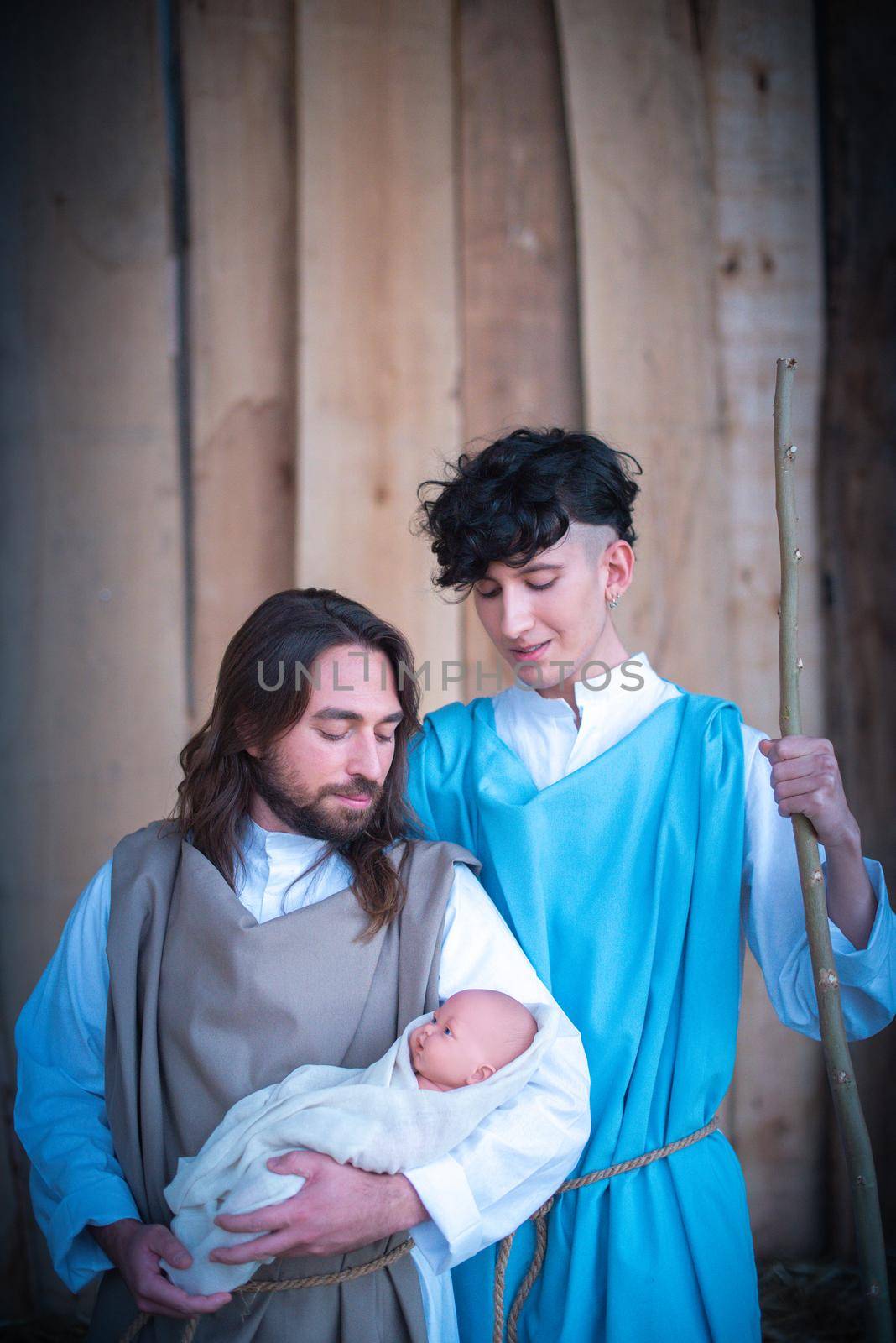 Vertical portrait of two men representing virgin mary and joseph in a nativity scene holding a baby