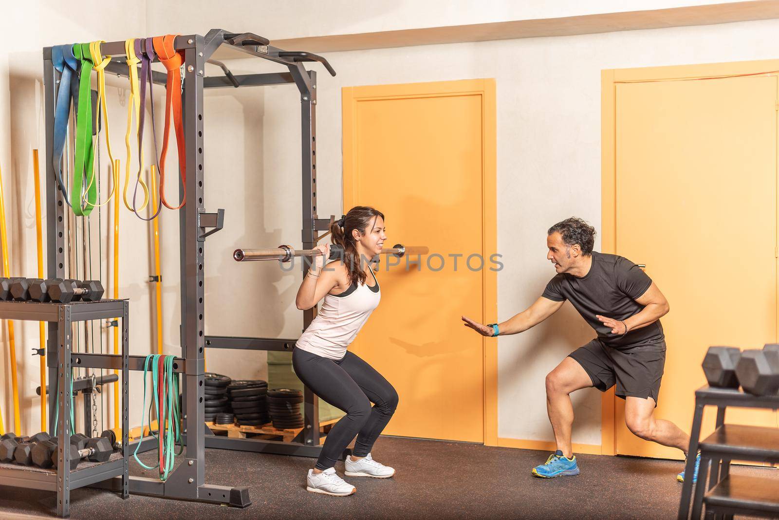 Sportswoman doing squats with bar with trainer in gym by ivanmoreno