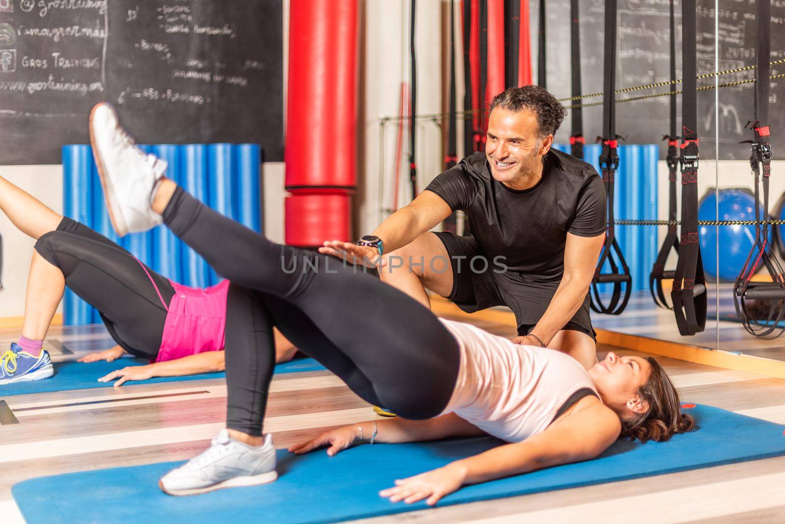 Women doing pelvic exercise with one leg up with help of trainer in gym. Concept of gym.