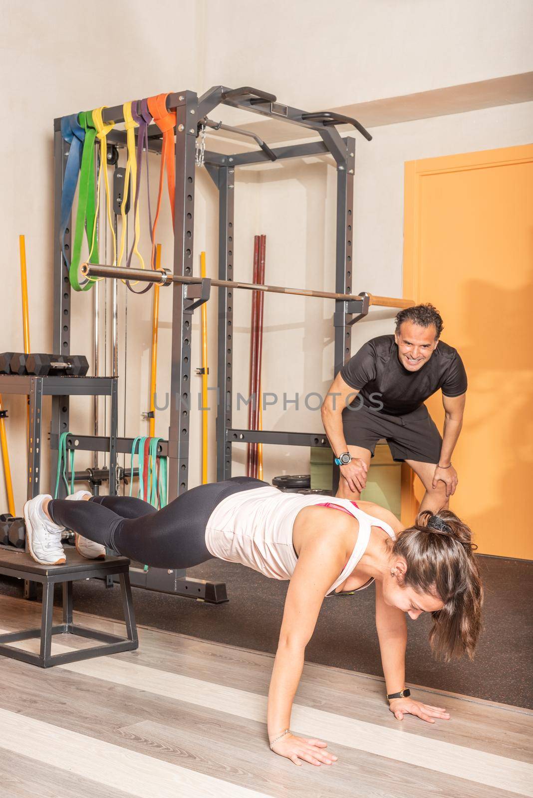 Sportswoman doing push ups with her feet on box with trainer in the gym. Concept of exercises in gym.