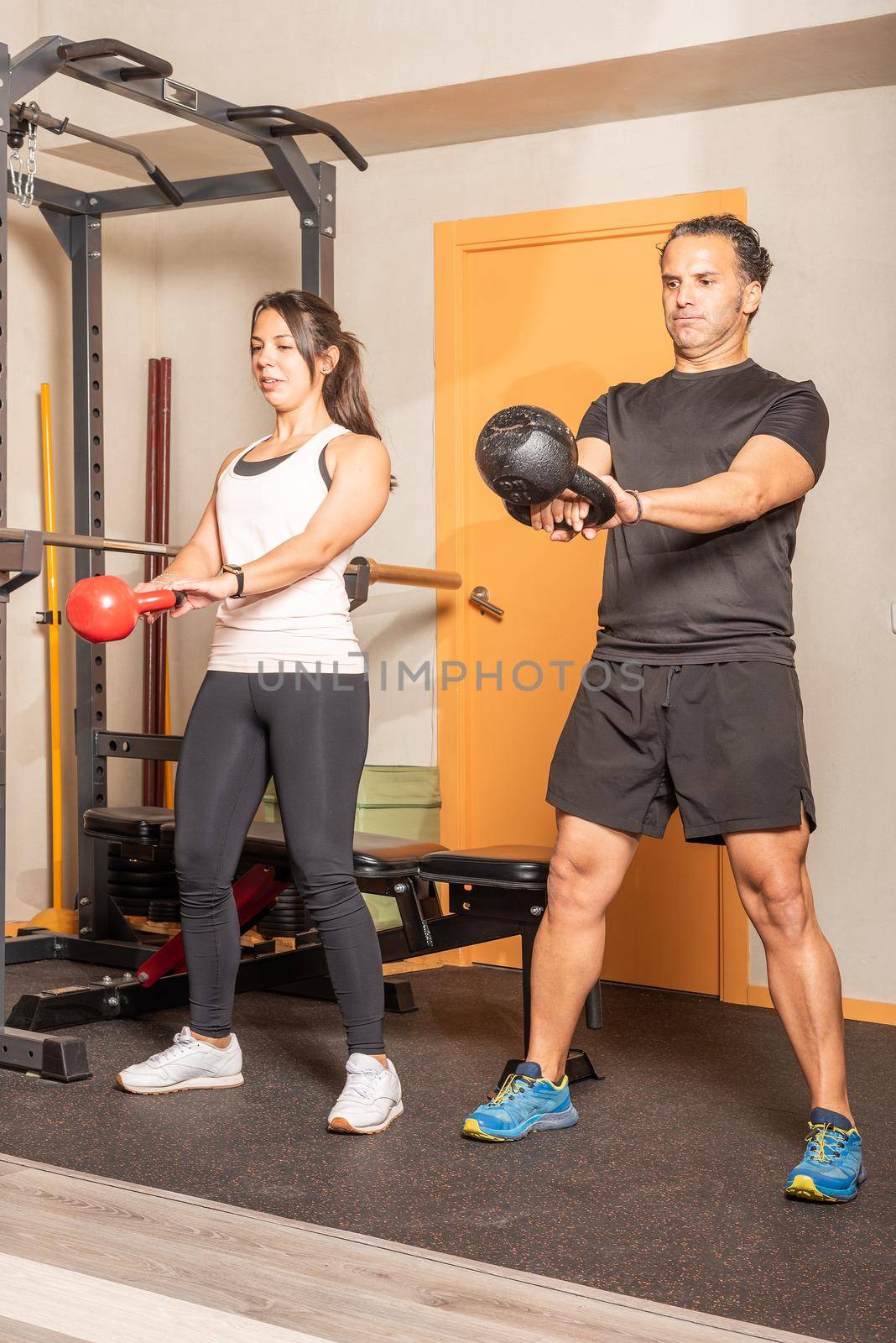 Sportswoman and man doing kettlebell swing exercise at gym. Concept of exercises with equipment in gym.