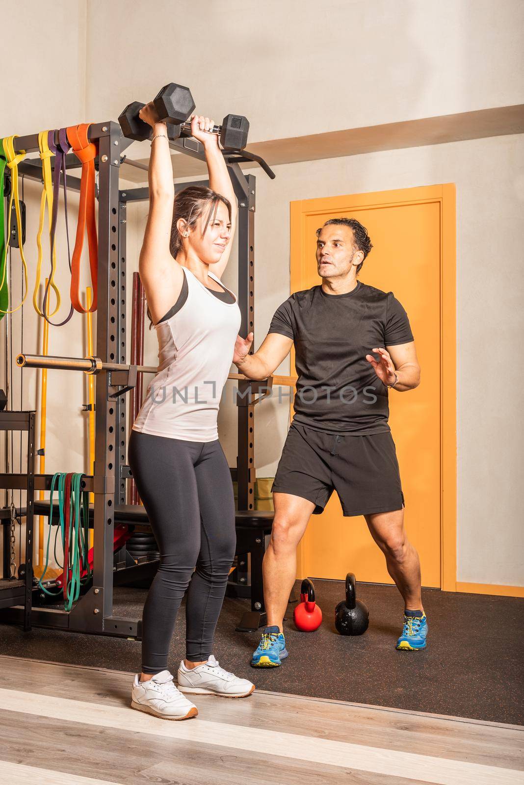 Woman doing shoulder exercise with dumbbells in the gym. Concept of exercise with equipment at gym.