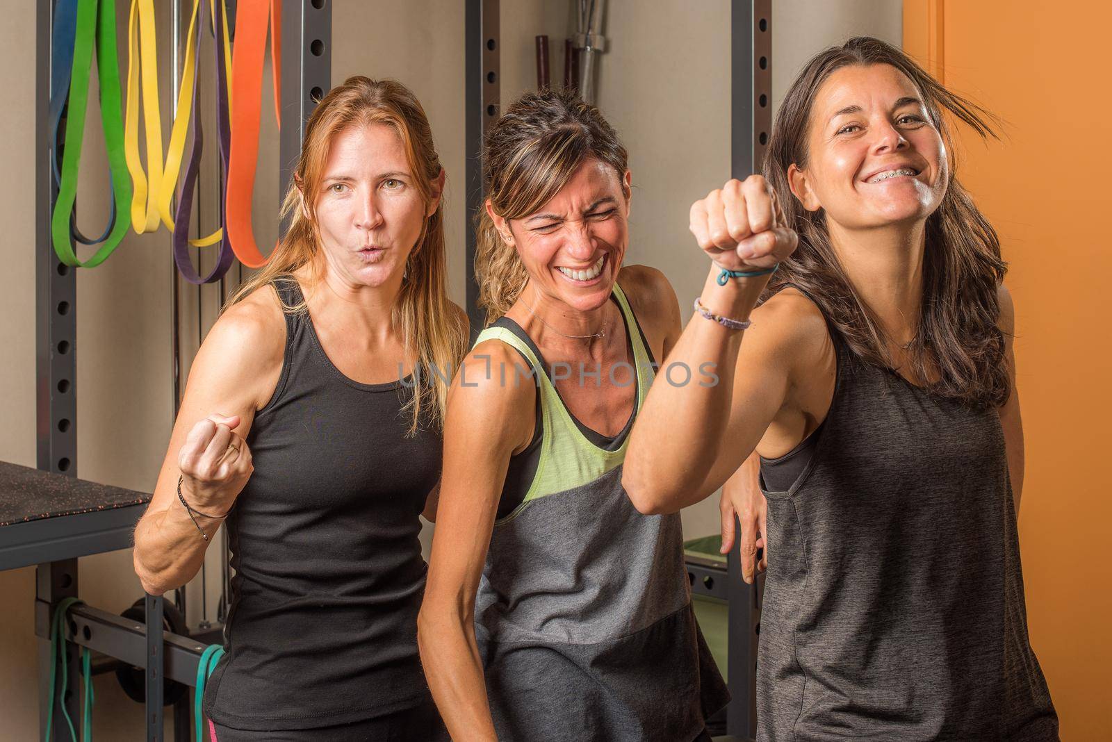 Portrait of three sportswoman showing closed fists in funny way in gym. Concept of people in gym.