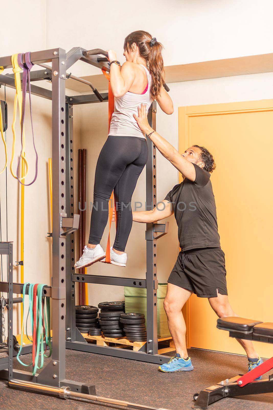 Athlete woman doing pull ups exercise with bar with help of trainer in gym by ivanmoreno