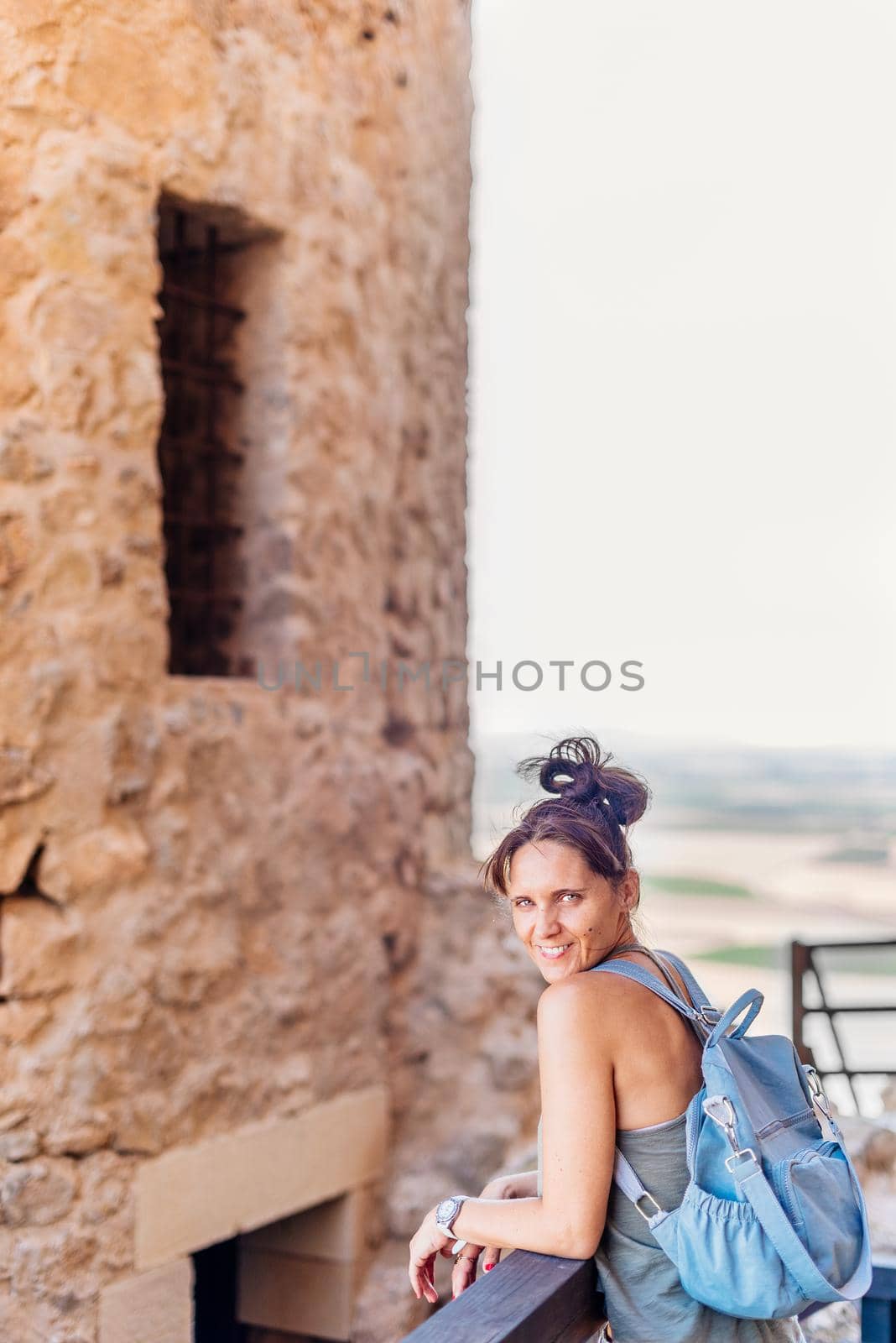 Vertical photo of a woman looking at the camera while leaning on a railing next to historic castle in Toledo, Spain.