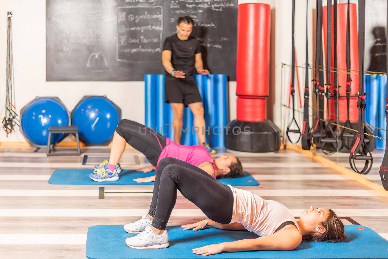 Women doing pelvic exercise with trainer in gym by ivanmoreno