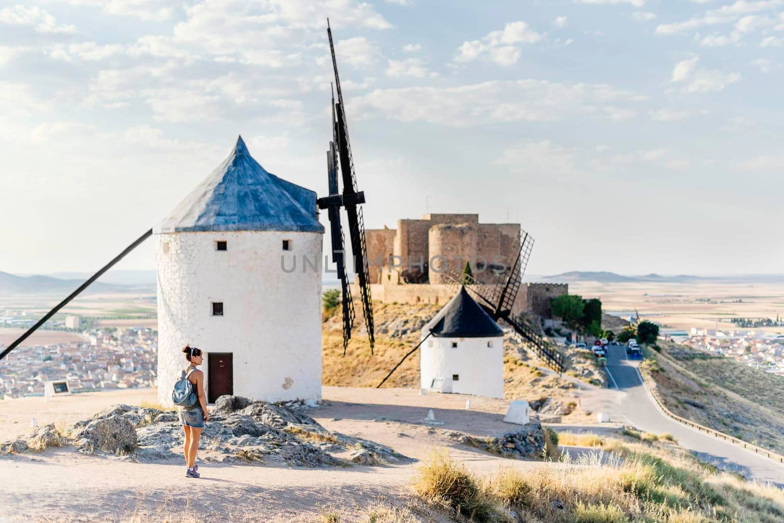 Tourist standing on a hill with a group of restored antique windmills and a castle in Consuegra, Toledo in Spain