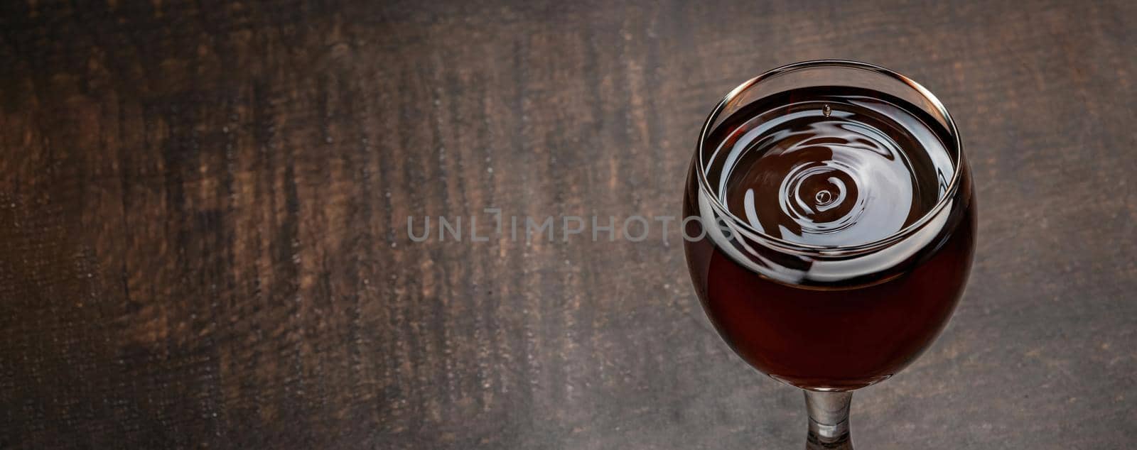 Drops of wine and waves forming in a glass full of red wine standing on a wooden table
