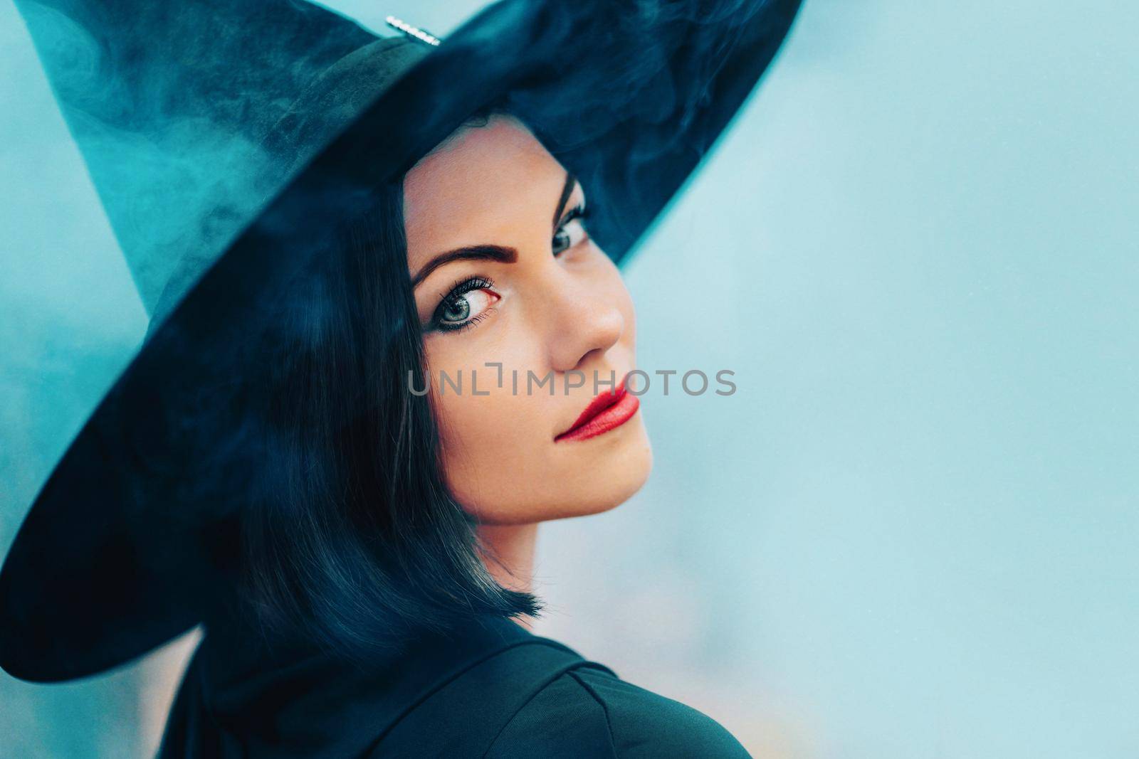 Portrait of woman as witch in black on blue fog, smoke background. Fairy tale concept, halloween, cosplay. by kristina_kokhanova
